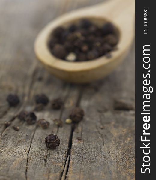 Pepper grains in the spoon on the wooden background. Pepper grains in the spoon on the wooden background