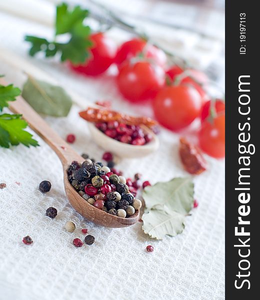 Various pepper in wooden spoon with tomato on background