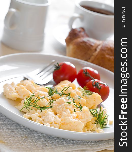 A plate of creamy scrambled eggs garnished with dill, a cup of coffee with milk. A plate of creamy scrambled eggs garnished with dill, a cup of coffee with milk