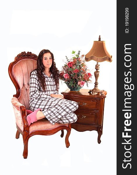 A young pretty woman in pyjamas, sitting in a pink armchair with an night stand and lamp for white background. A young pretty woman in pyjamas, sitting in a pink armchair with an night stand and lamp for white background.