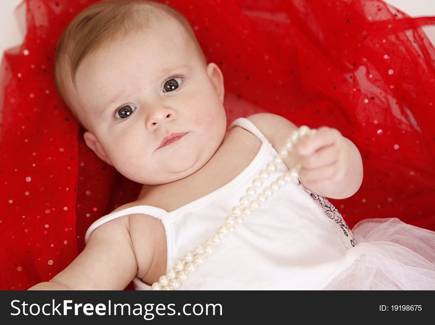 A baby girl plays with beads on a red blanket. Studio shot. A baby girl plays with beads on a red blanket. Studio shot.