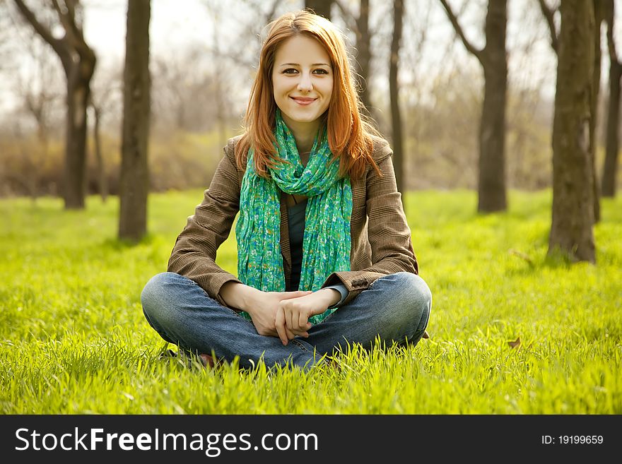 Beautiful girl sitting at green grass at park.