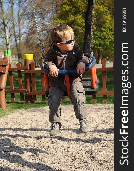 Young boy with sunglasses sitting on a swing and having fun on a playground. Young boy with sunglasses sitting on a swing and having fun on a playground