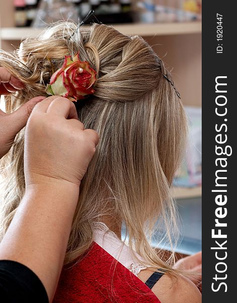 At the hairdresser. The hairdresser is pinning the rose up into hair. At the hairdresser. The hairdresser is pinning the rose up into hair