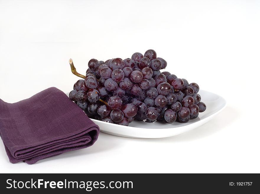 A Bunch Of Juicy Red Grapes On A White Plate With A Purple Napki