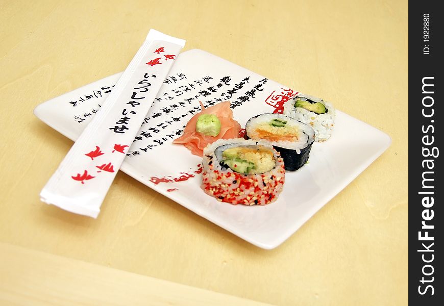 Pieces of sushi (sashimi) on a white plate with Japanese (kanji) writing. Includes chopsticks, wasabi paste and pickled ginger. Close Up. Pieces of sushi (sashimi) on a white plate with Japanese (kanji) writing. Includes chopsticks, wasabi paste and pickled ginger. Close Up.