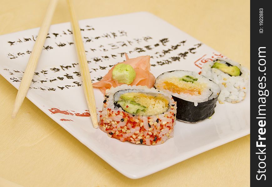 Pieces of sushi (sashimi) on a white plate with Japanese (kanji) writing. Includes chopsticks, wasabi paste and pickled ginger. Close Up. Pieces of sushi (sashimi) on a white plate with Japanese (kanji) writing. Includes chopsticks, wasabi paste and pickled ginger. Close Up.