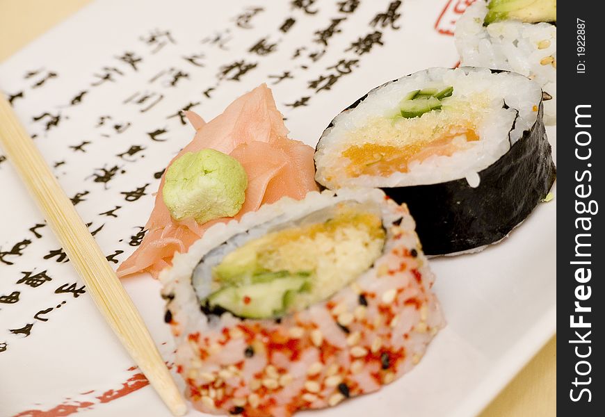 Pieces of sushi (sashimi) on a white plate with Japanese (kanji) writing. Includes chopsticks, wasabi paste and pickled ginger. Close Up. Pieces of sushi (sashimi) on a white plate with Japanese (kanji) writing. Includes chopsticks, wasabi paste and pickled ginger. Close Up.