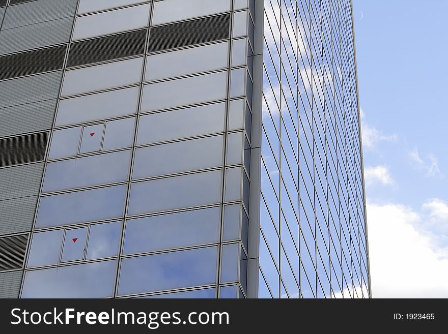 Detail of a corporate building with windows and cloudy sky reflections