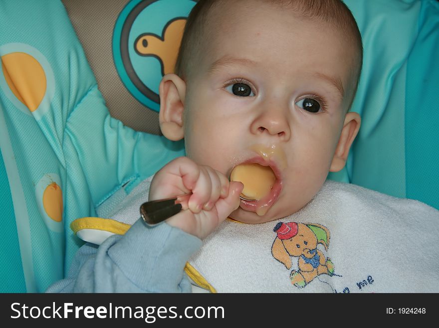 The kid of 7 months sits with the spoon. The kid of 7 months sits with the spoon