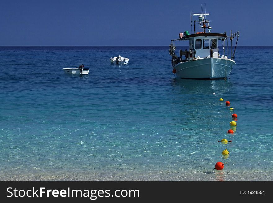 Three boats at sea with blue sky and color buoy.