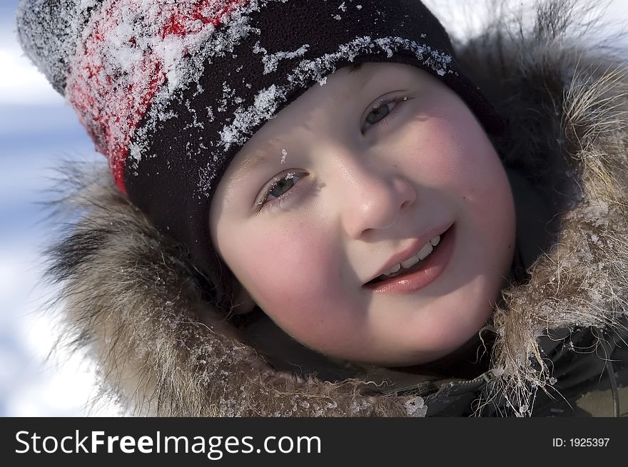 Portrait of young smiling boy in winter clothes and hat covered with snow taken in sunny, cold winter day. Portrait of young smiling boy in winter clothes and hat covered with snow taken in sunny, cold winter day