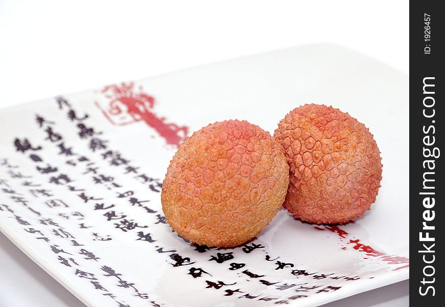 Two Lychee (litchi) placed on a white plate with Japanese (kanji) writing. Close Up. Two Lychee (litchi) placed on a white plate with Japanese (kanji) writing. Close Up.