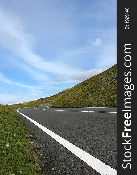 Uphill road in deserted countryside with grass verges either side with a blue sky with clouds. Set in the Brecon Beacons, National Park, Wales, United Kingdom. Uphill road in deserted countryside with grass verges either side with a blue sky with clouds. Set in the Brecon Beacons, National Park, Wales, United Kingdom.