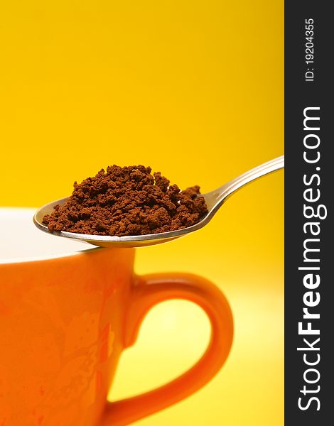 Closeup of spoon with instant coffee and cup on yellow background