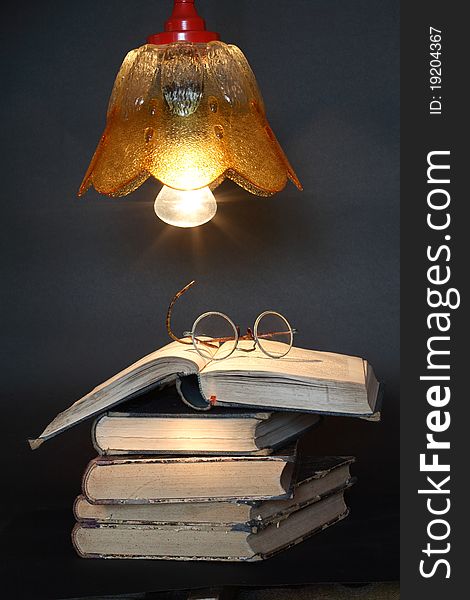 Stack of old books and spectacles under luminous lamp. Stack of old books and spectacles under luminous lamp