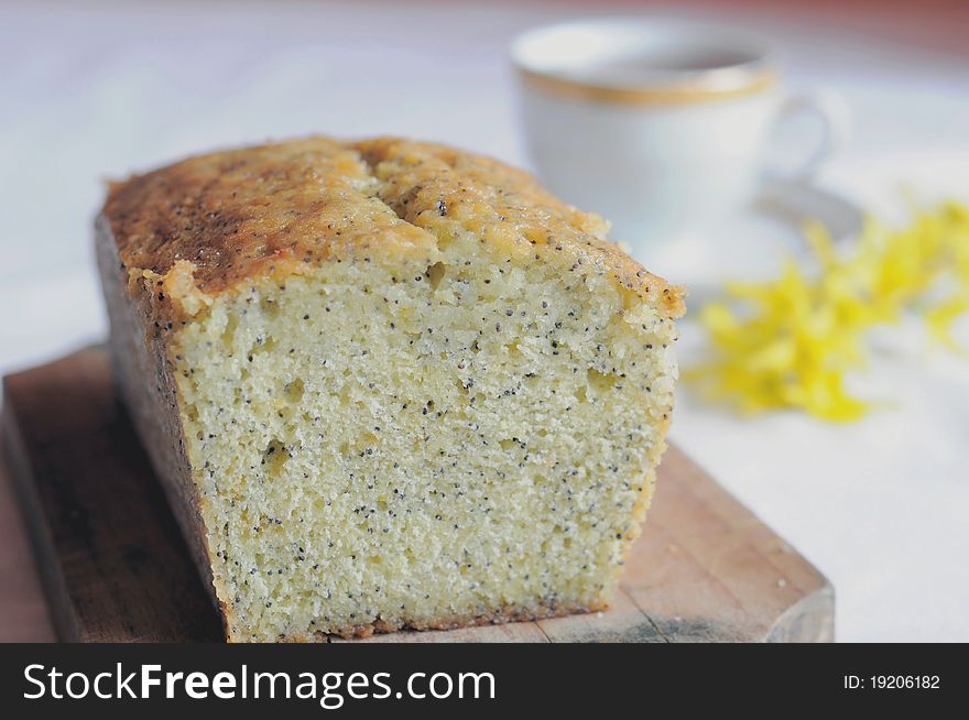 Delicious lemon cake with poppy seeds, yellow flowers and a cupt of tea in the background