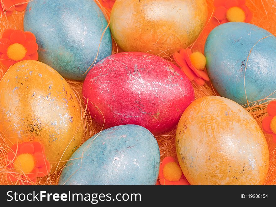 Shiny multicolored easter eggs on orange straw with flowers.
