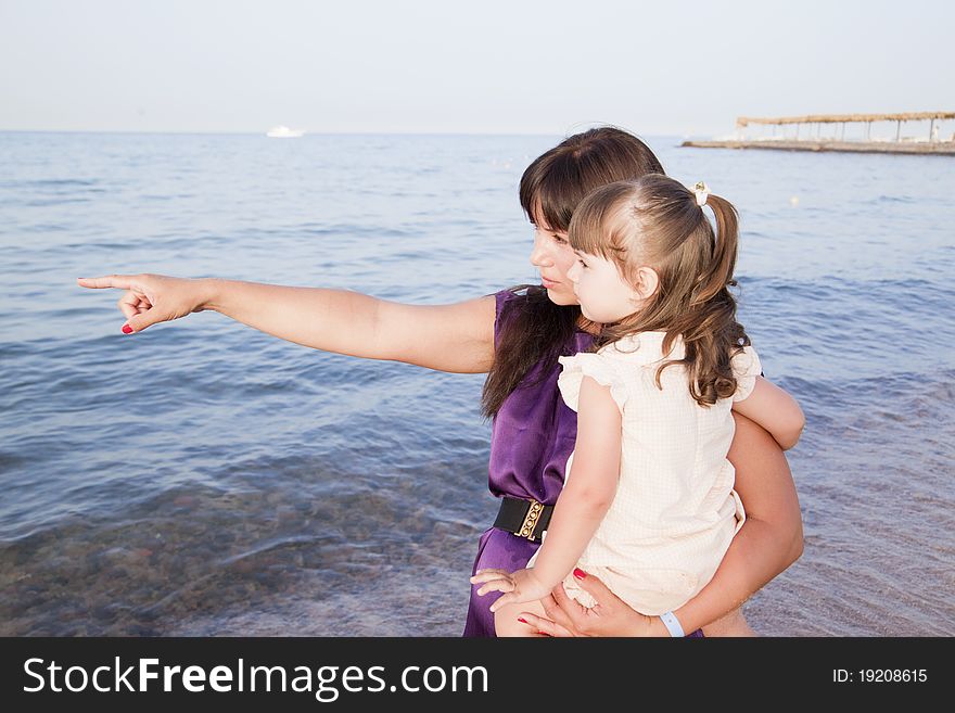 Mom hugs her daughter and shows on the sea. Mom hugs her daughter and shows on the sea