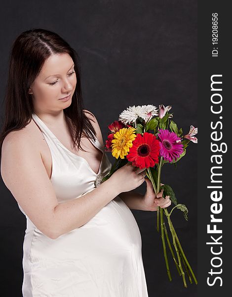 Pregnant woman in a white dress looking at a bouquet gerbera