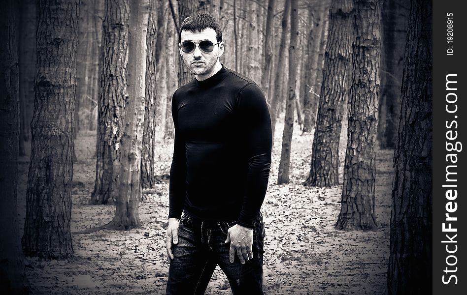 Young man in black clothes and sunglasses at forest