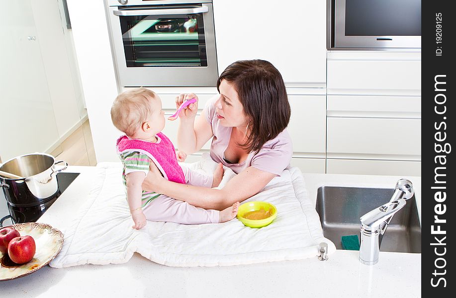 Young mother is feeding her baby in a modern kitchen setting. Young mother is feeding her baby in a modern kitchen setting.