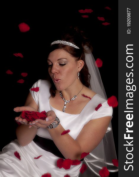 A bride holding rose petals in her hands blowing on them as they fly over her head. A bride holding rose petals in her hands blowing on them as they fly over her head.