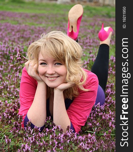 Young beautiful blond cheerful woman laying on blooming field in spring. Young beautiful blond cheerful woman laying on blooming field in spring