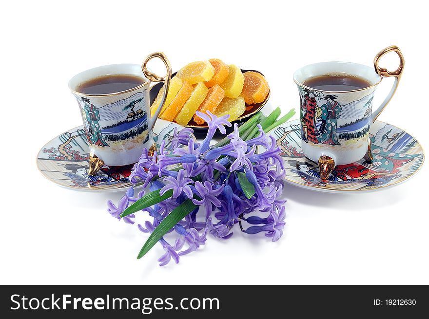 Two cups of coffee with flowers and fruit jellies are isolated on a white background