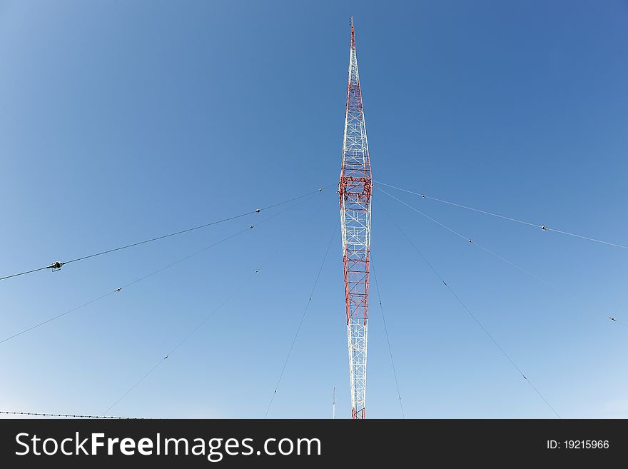 A red and white weather station antenna with guide wires and lightning arresters. All against a clear, deep blue sky.