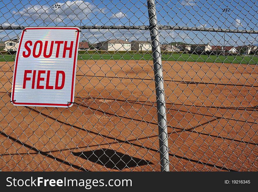 A view of a softball field from behind home plate, looking through the back stop.