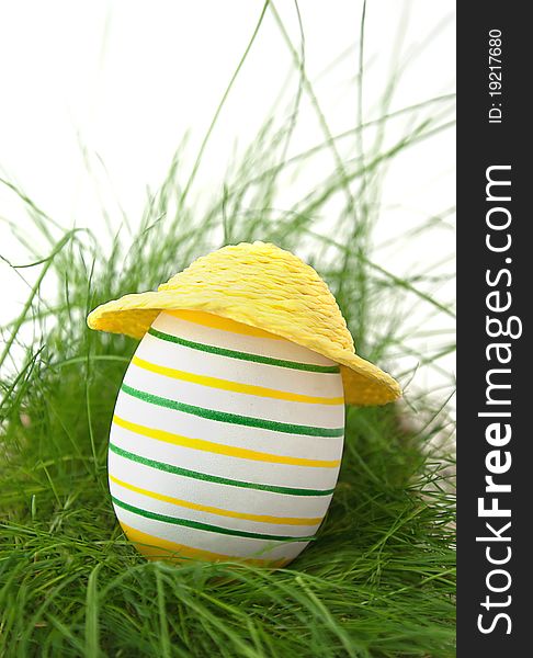 Easter egg in straw yellow hat in green grass