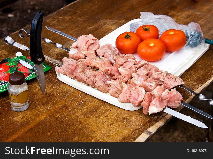 On a wooden table prepared with raw meat skewers for shish kebab and tomato