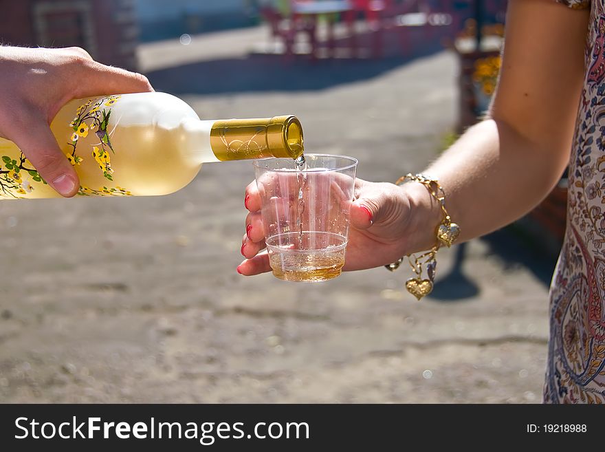 From the sun-lit bottles of hand pours wine into a glass. From the sun-lit bottles of hand pours wine into a glass