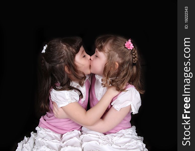 Adorable twin girls kissing each other on black. Adorable twin girls kissing each other on black