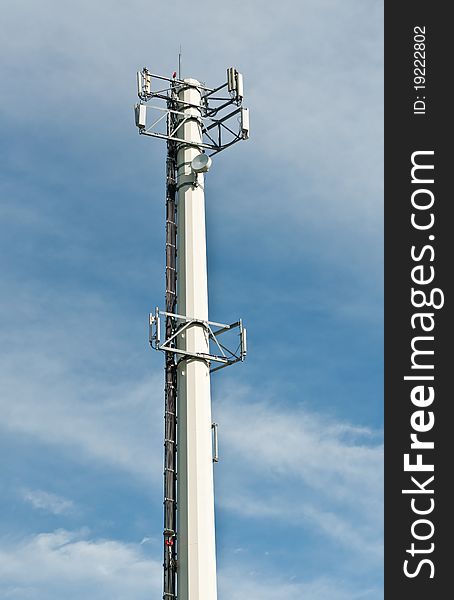 A telecom antenna tower stands out against a blue sky with white clouds.