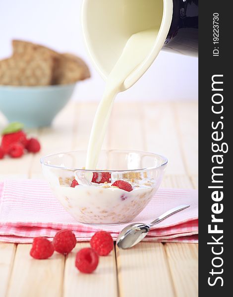 Pouring milk on a bowl of cereal (muesli/granola) with fresh strawberries, raspberries and fruit in the background. Pouring milk on a bowl of cereal (muesli/granola) with fresh strawberries, raspberries and fruit in the background.