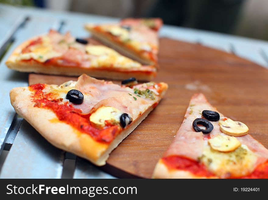 Sliced pizza with ham and olives on a wooden board