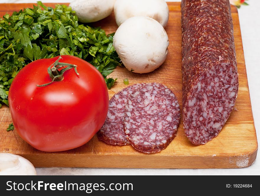 Some ingredients for pizza: parsley, sausage, tomatoes.