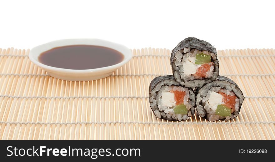 Three roll and a plate with soy sauce out of focus  on a bamboo mat. Three roll and a plate with soy sauce out of focus  on a bamboo mat.