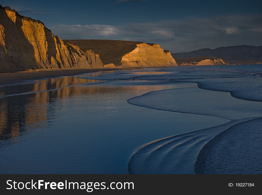 A bright orange sunset is reflected on the coastal cliffs of Drakes Beach. A bright orange sunset is reflected on the coastal cliffs of Drakes Beach