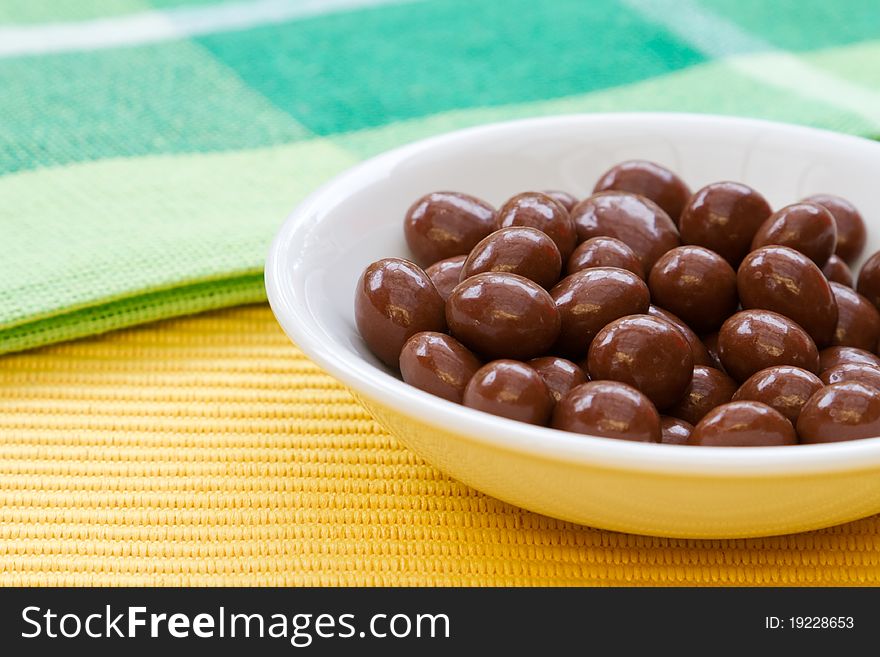 Chocolate sultanas in white bowl on yellow tablecloth.