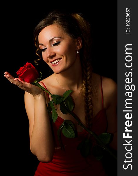 Smiling girl looking at a red rose on a black background. Smiling girl looking at a red rose on a black background