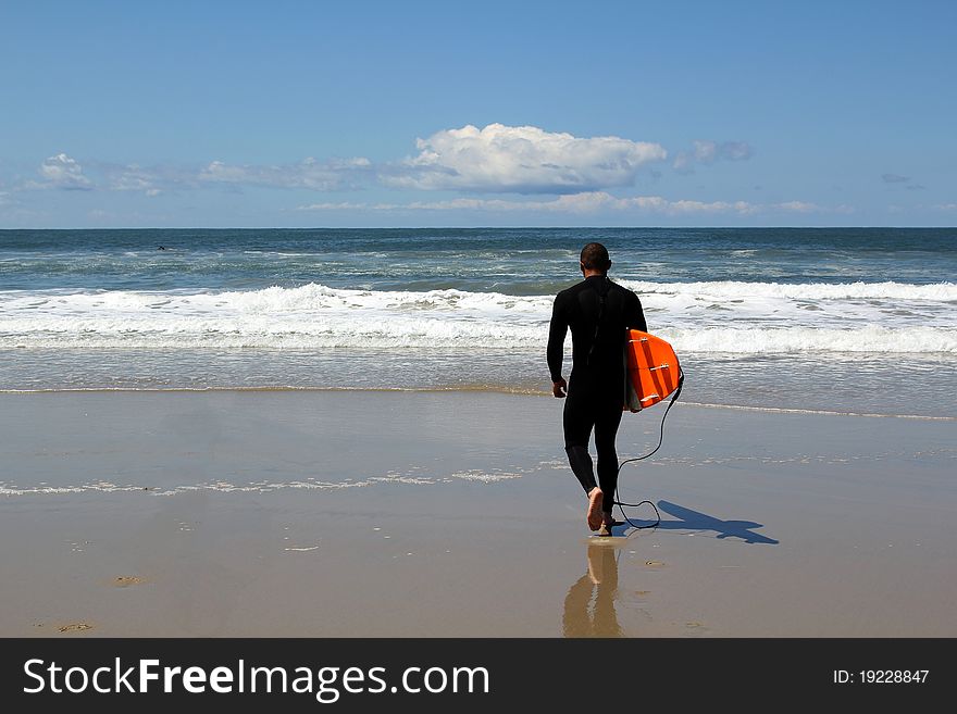 Man in wetsuit heads out to surf on the California coast. Man in wetsuit heads out to surf on the California coast