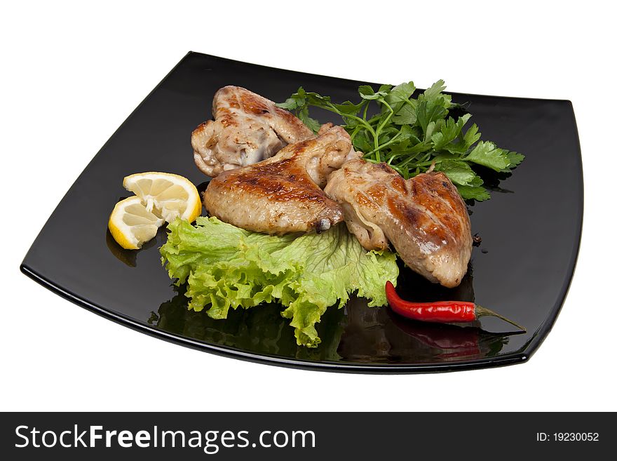 Chicken wings grilled with herbs, pepper and lemon on a black plate. Isolation on bedlm background.