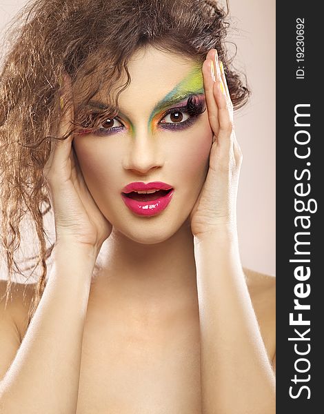 Beautiful young attracive female face with bright fashion multicolored make-up and beauty yellow manicure of fingernails