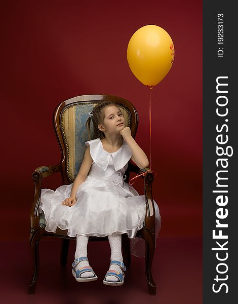 Studio portrait of a young pretty girl sitting on the armchair and with yellow balloon. Studio portrait of a young pretty girl sitting on the armchair and with yellow balloon