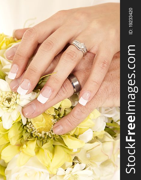 A bride and goom with their hands on top of the flowers, showing off their rings. A bride and goom with their hands on top of the flowers, showing off their rings.