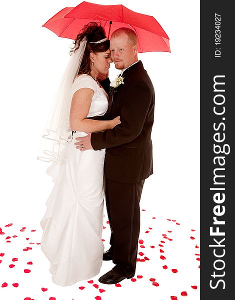 A bride and groom under a red umbrella standing in rose petals.