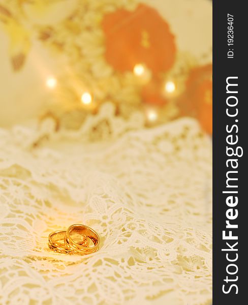 Gold wedding bands on white lace with candles and orange accents